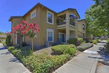A yellow two-story house with a balcony and a flower bed in front.